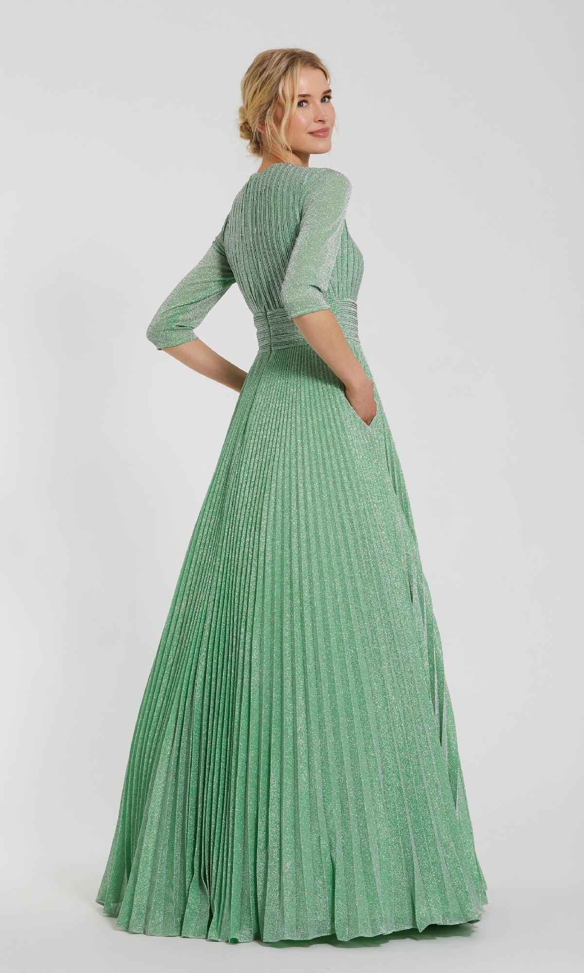 A woman faces away, wearing the Sage Long Pleated Formal Dress by Mac Duggal (30775), featuring three-quarter sleeves and a shimmering pleated A-line silhouette.